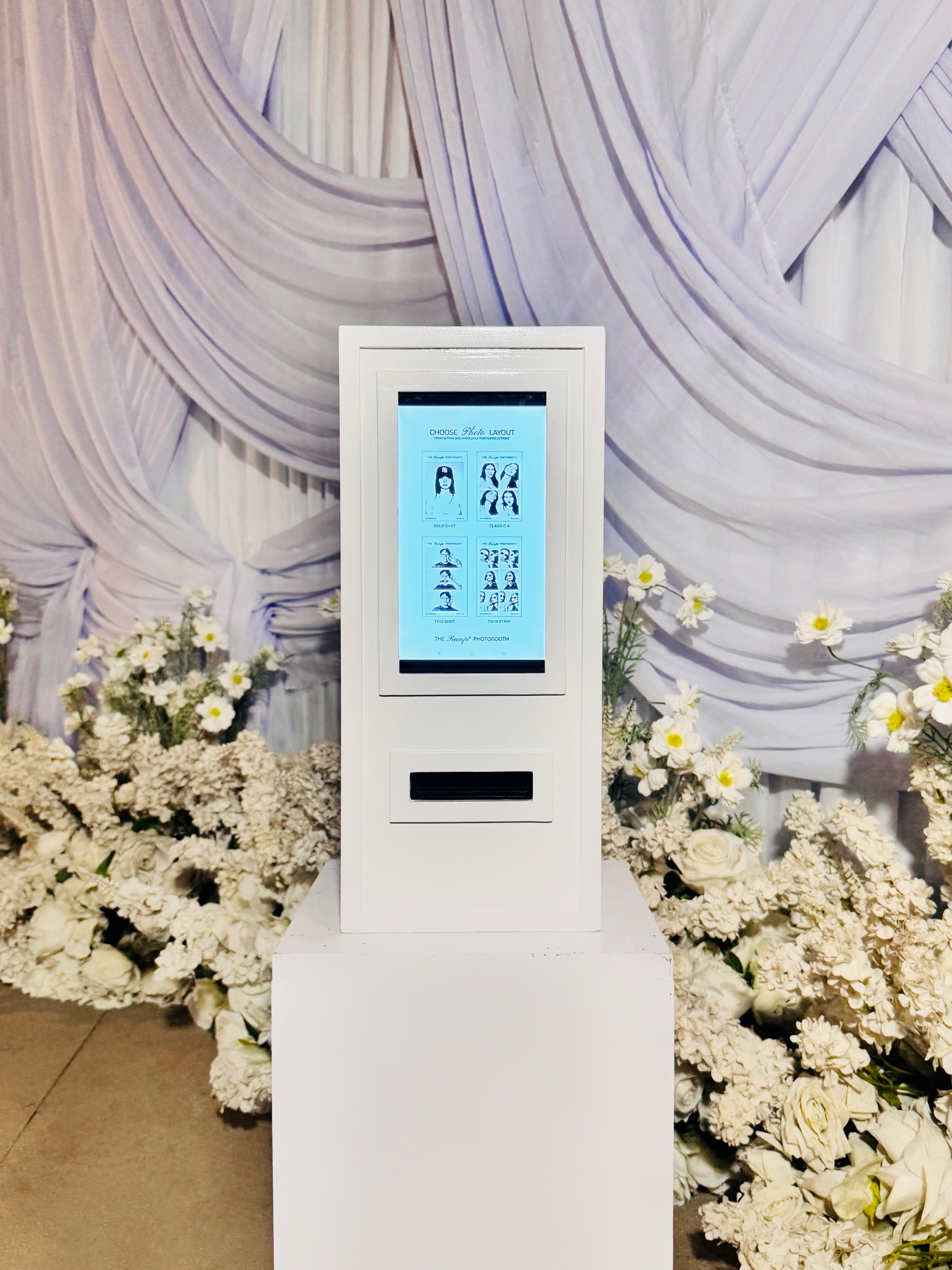 The booth beside white draping and a large white floral arrangement at a wedding